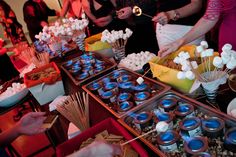 several people standing around a table filled with cupcakes and marshmallows