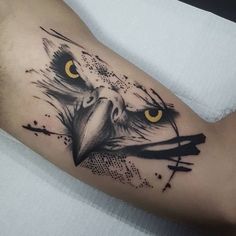 an eagle tattoo on the arm with yellow eyes and black ink splatters around it