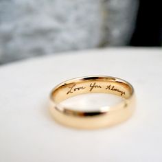 a gold wedding ring with the words i love you mom on it sitting on a table