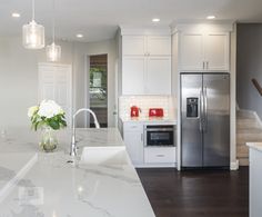 a white kitchen with marble counter tops and stainless steel refrigerator freezer next to stairs