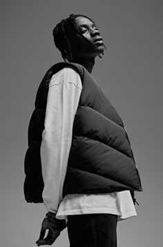 a man with dreadlocks wearing a puffy vest and standing in front of a gray sky