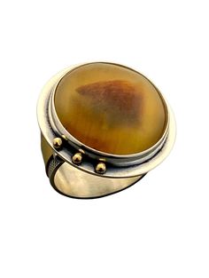 Gold, Silver & Stone Ring - Showcasing a Brazilian agate, this one of a kind ring was created in sterling silver and 18k gold. The 20mm cabochon has enchanting orange undertones and the ring is a size 8 with a 10mm textured band. Unique Polished Moonstone Ring, Amber Cabochon Ring, Gold Agate Cabochon Rings, Amber Agate Cabochon Ring, Unique Cabochon Chalcedony Ring, Orange Cabochon Sterling Silver Jewelry, Unique Orange Cabochon Ring, Vintage Orange Cabochon Rings, Brazilian Agate