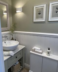 a white sink sitting next to a mirror in a bathroom under two framed pictures on the wall