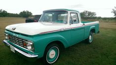 an old green and white truck is parked in the grass