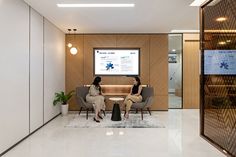 two women sitting in chairs with a projector screen on the wall behind them,