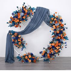 an orange and blue floral wreath is hanging on the wall next to a gray drape