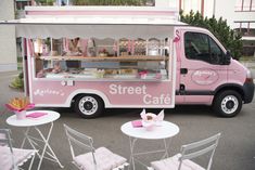 a pink food truck parked in front of a building with tables and chairs around it