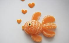 an orange fish made out of fruit on a white surface with hearts in the background