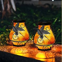 two lit candles sitting on top of a table next to some plants and flowers in the background