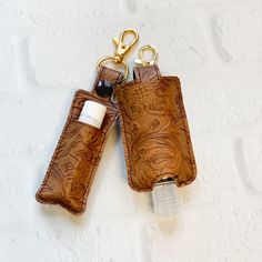 two brown leather keychains hanging on a white brick wall with a bottle in it