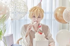 a person sitting at a table with a cake in front of them and balloons all around