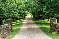 a dirt road surrounded by lush green trees and stone pillars with statues on each side