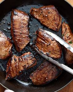 steak being cooked in a skillet with tongs