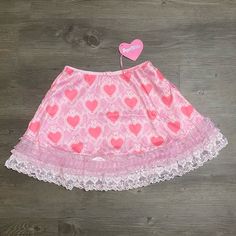 This Mini Skirt Has An All Over Hearts, Bows, And Pearls Graphic Print, A Lace And Ruffle Trim, A Low Waist Fit, And A Back Zip Closure. Cute Pleated Mini Skirt, White Mini Skirt In Fairy Kei Style, Fairy Kei White Mini Skirt, White Fairy Kei Mini Skirt, Fairy Kei Pink Tiered Skirt, Pink Fairy Kei Tiered Skirt, Pink Fairy Kei Mini Skirt, Cute White Skirted Skort, Pink Mini Skirt With Lace Trim