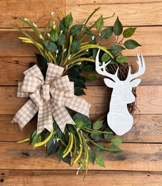 a wreath with deer head and antlers on it sitting on a wooden floor next to a pine cone