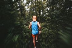 a man in blue shirt and orange shorts running through trees