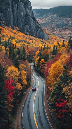 a car driving down a road surrounded by trees with fall foliage on the mountains in the background