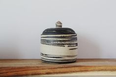 a black and white ceramic jar sitting on top of a wooden table next to a wall