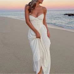 a woman standing on top of a beach next to the ocean wearing a white dress