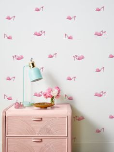 a pink dresser with a lamp on top and wallpaper in the shape of high heel shoes