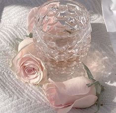 a glass vase sitting on top of a table next to pink flowers and white cloth