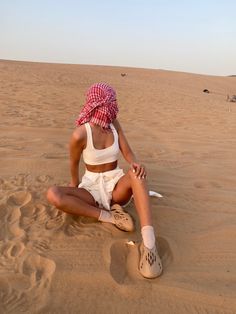 a woman sitting on top of a sandy beach next to a white frisbee