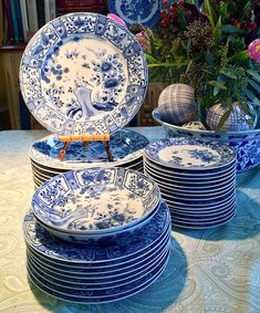 blue and white plates stacked on top of each other in front of a vase with flowers