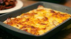 a casserole dish on a table with other food items in the back ground