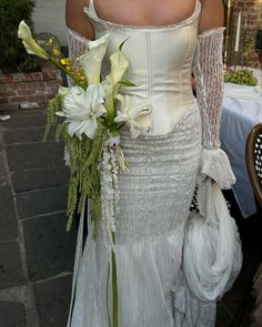 a woman in a white wedding dress holding a bouquet of flowers and wearing a lace corset