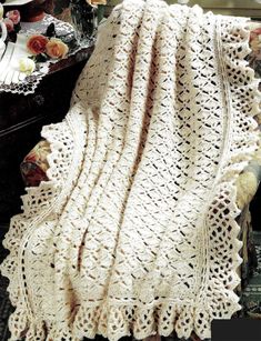 a white crocheted blanket sitting on top of a table next to a vase with flowers