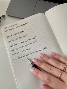 a woman's hand holding a pen next to an open notebook with writing on it