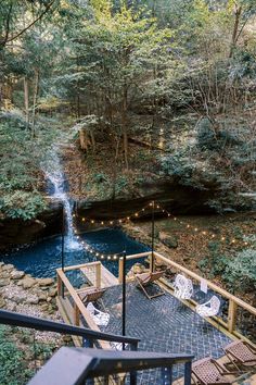 a wooden deck with chairs and lights next to a small waterfall in the middle of a forest