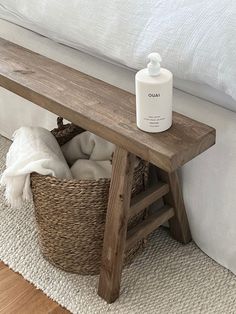 a white bottle sitting on top of a wooden bench next to a basket filled with blankets