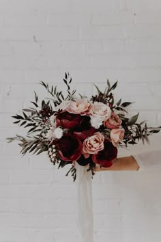 a woman holding a bouquet of red and white flowers in front of a brick wall