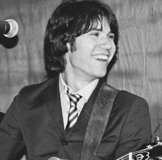 a man in a suit playing an acoustic guitar and singing into a microphone behind him