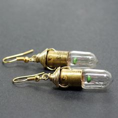 two clear glass and gold tone earrings on a black surface, one with green accents