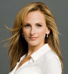 a woman with long blonde hair wearing a white shirt and diamond earrings, posing for a headshot