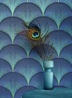 a vase with a peacock feather on top of it next to a blue wallpaper