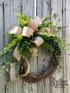 a wreath is hanging on the side of a wooden fence with greenery and burlocks