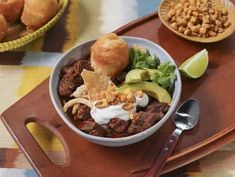 a bowl filled with meat and vegetables on top of a wooden tray next to bread