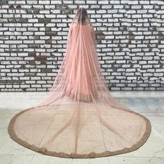 a woman wearing a pink veil standing in front of a brick wall with her back turned to the camera