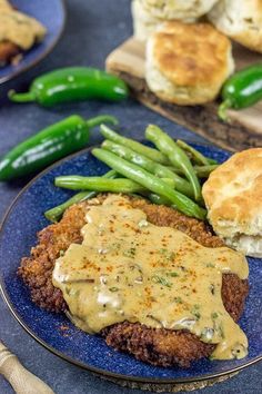 a blue plate topped with meat covered in gravy next to green beans and biscuits