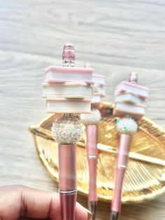 three pink pens with glitter on them sitting in front of a gold plated object