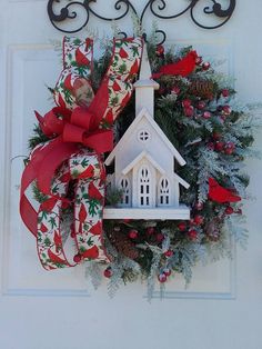 a wreath with a birdhouse hanging from it's side and a red bow on the front door