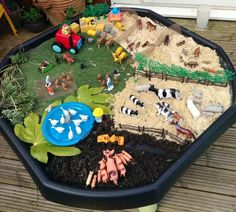 an outdoor play area with toy farm animals and toys in the dirt, on a wooden deck