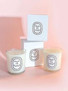 two candles sitting next to each other in front of a white box on a pink background