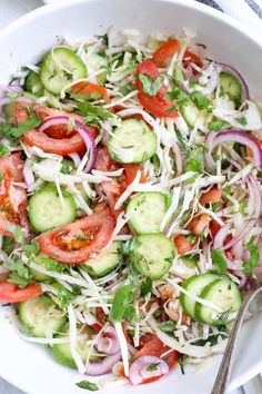 a white bowl filled with cucumber, tomatoes and onions next to a spoon