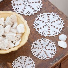 white crocheted doily and seashells in a bowl on a wooden table