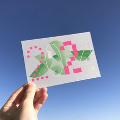 a hand holding up a piece of paper with geometric designs on it and a blue sky in the background