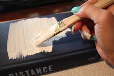 a person holding a paintbrush over a book with white paint on it and the word distance written in gold